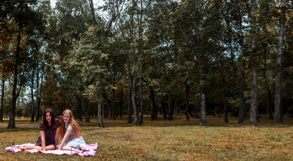 two girls sitting on a blanket in the woods