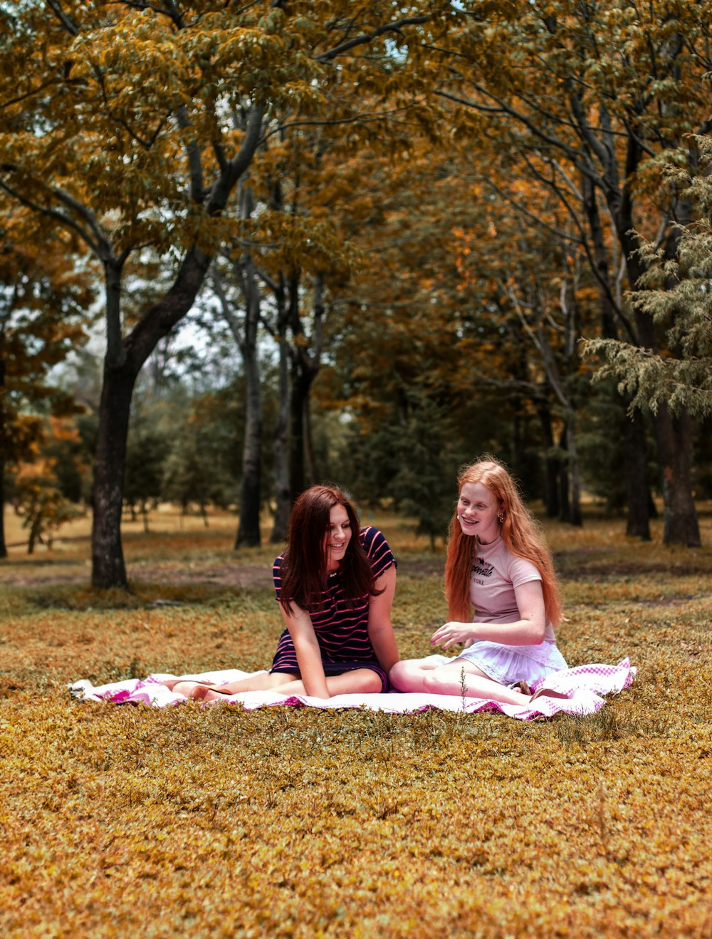 two girls sitting on a blanket in a park