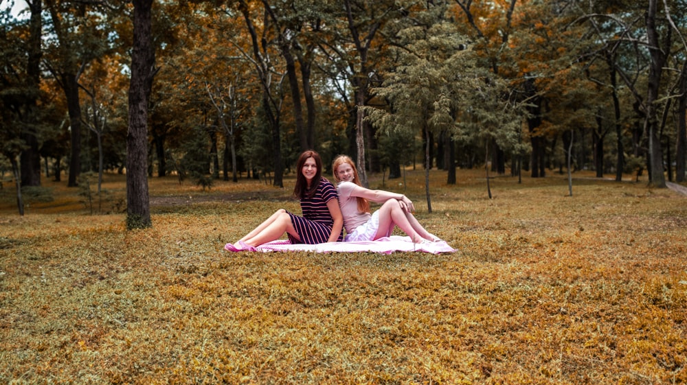 two women sitting on a blanket in the woods