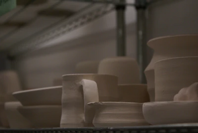 Ceramic pieces with earthy glazes drying on wooden shelves in a sunlit studio.