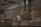 Several pieces of unglazed pottery are arranged on a metal shelf. The pottery includes bowls, cups, and vases, all with a smooth, light beige surface. The lighting is dim, creating a soft shadow across the objects, which appear to be works in progress or ready for further finishing.