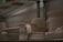 Several pieces of unglazed pottery are arranged on a metal shelf. The pottery includes bowls, cups, and vases, all with a smooth, light beige surface. The lighting is dim, creating a soft shadow across the objects, which appear to be works in progress or ready for further finishing.