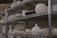 Metal shelves filled with various pottery items, including bowls, vases, and pots in different shapes and sizes. The pottery appears to be unfinished or in different stages of completion, with a predominantly matte finish.