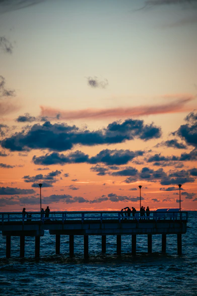 a group of people standing on a pier at sunset