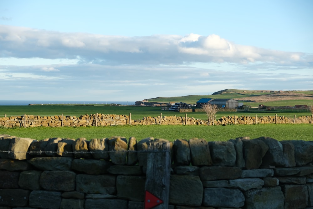 a stone wall in a field with a farm in the background