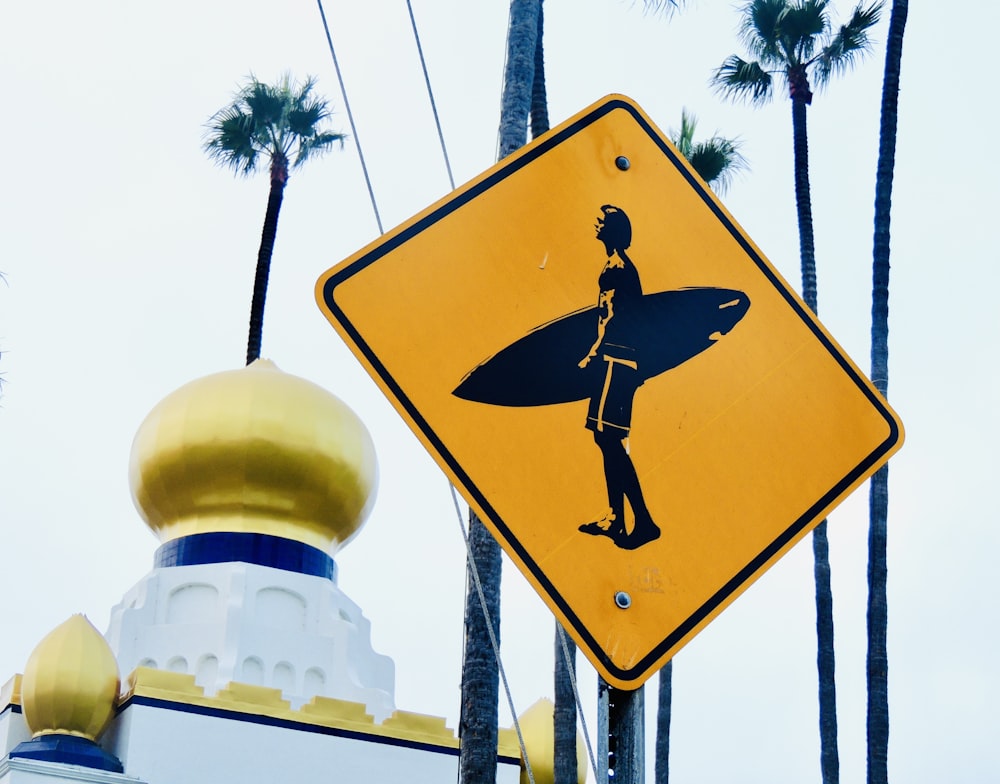 서핑보드를 들고 있는 사람의 사진이 있는 노란색 거리 표지판