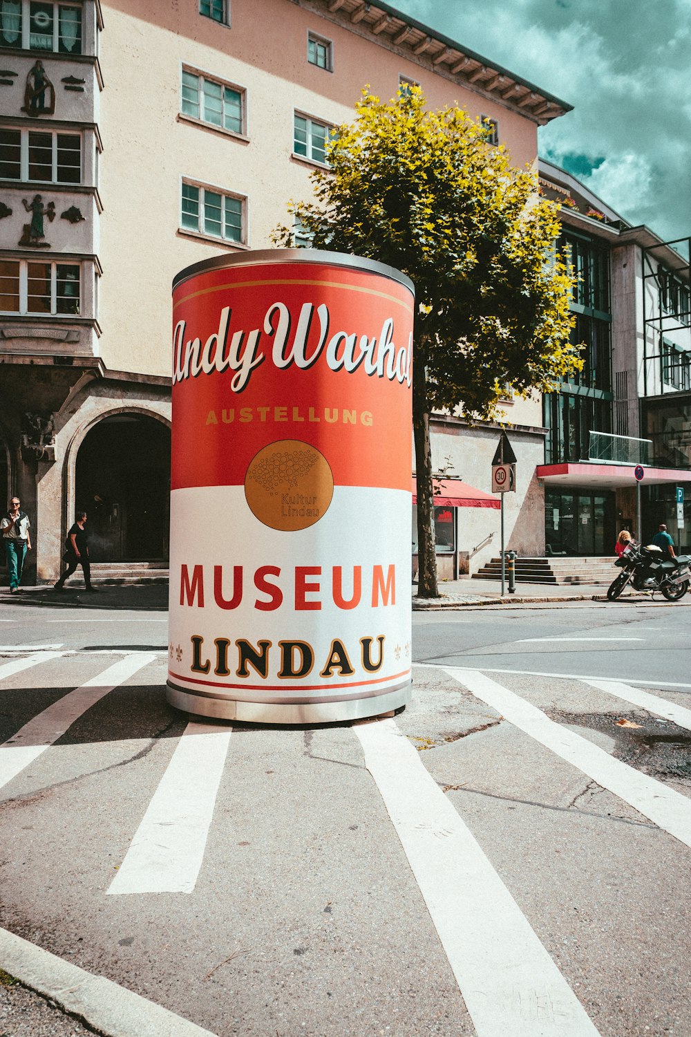 a red and white paint can sitting on the side of a road