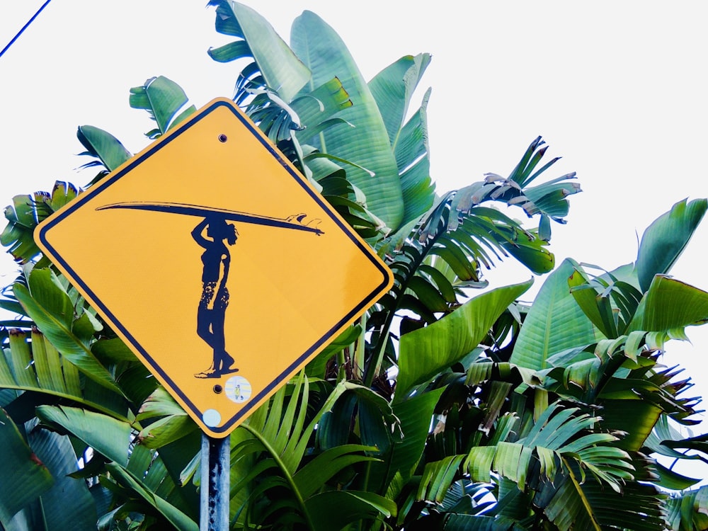 a yellow street sign with a man holding a surfboard on his head