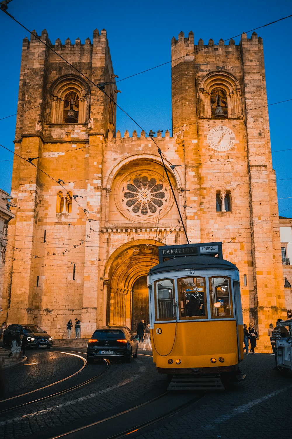 a yellow trolley driving past a tall stone building