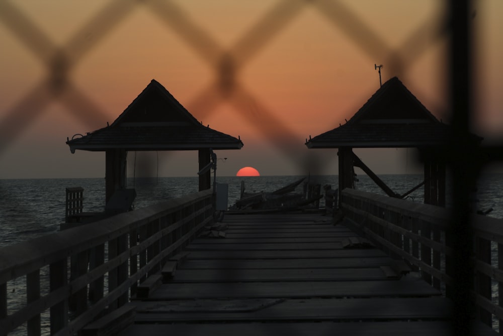 the sun is setting over the water from a pier