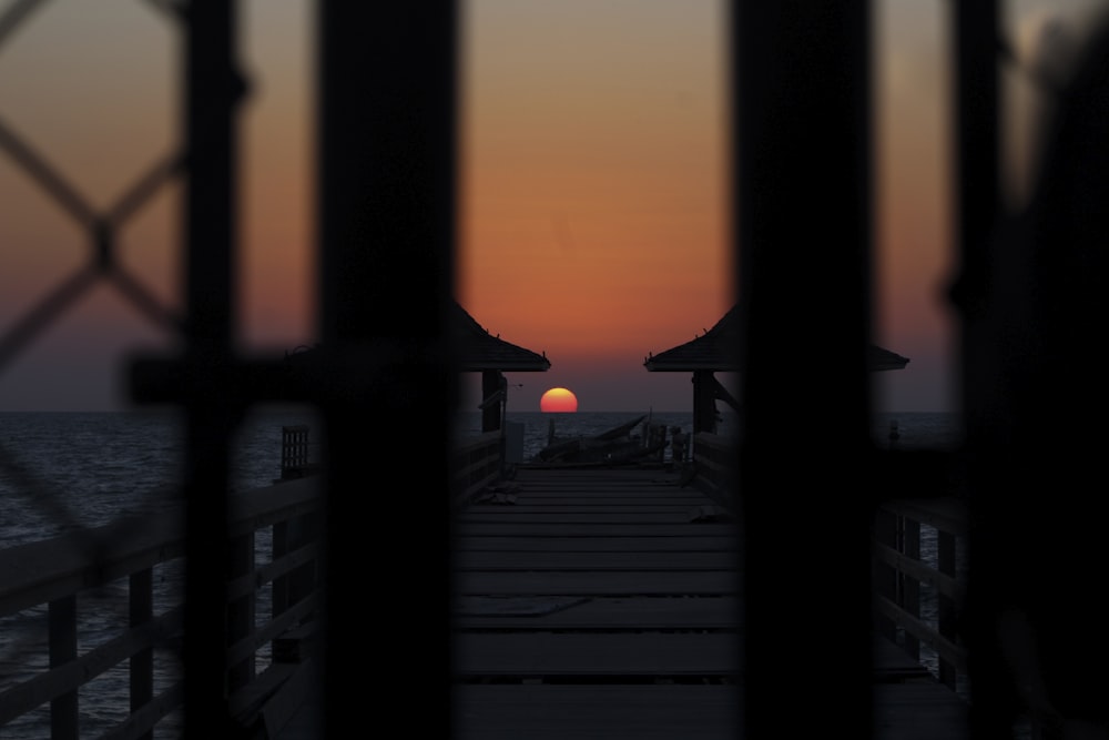 the sun is setting over the ocean from a pier