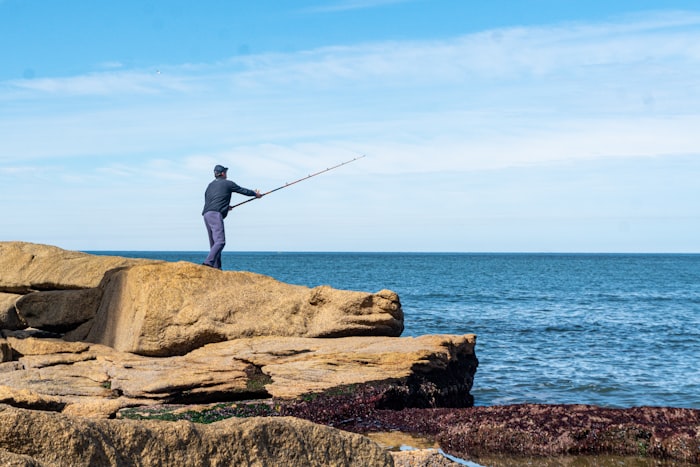 Angler fishing from a rocky shoreline at golden hour without a boat