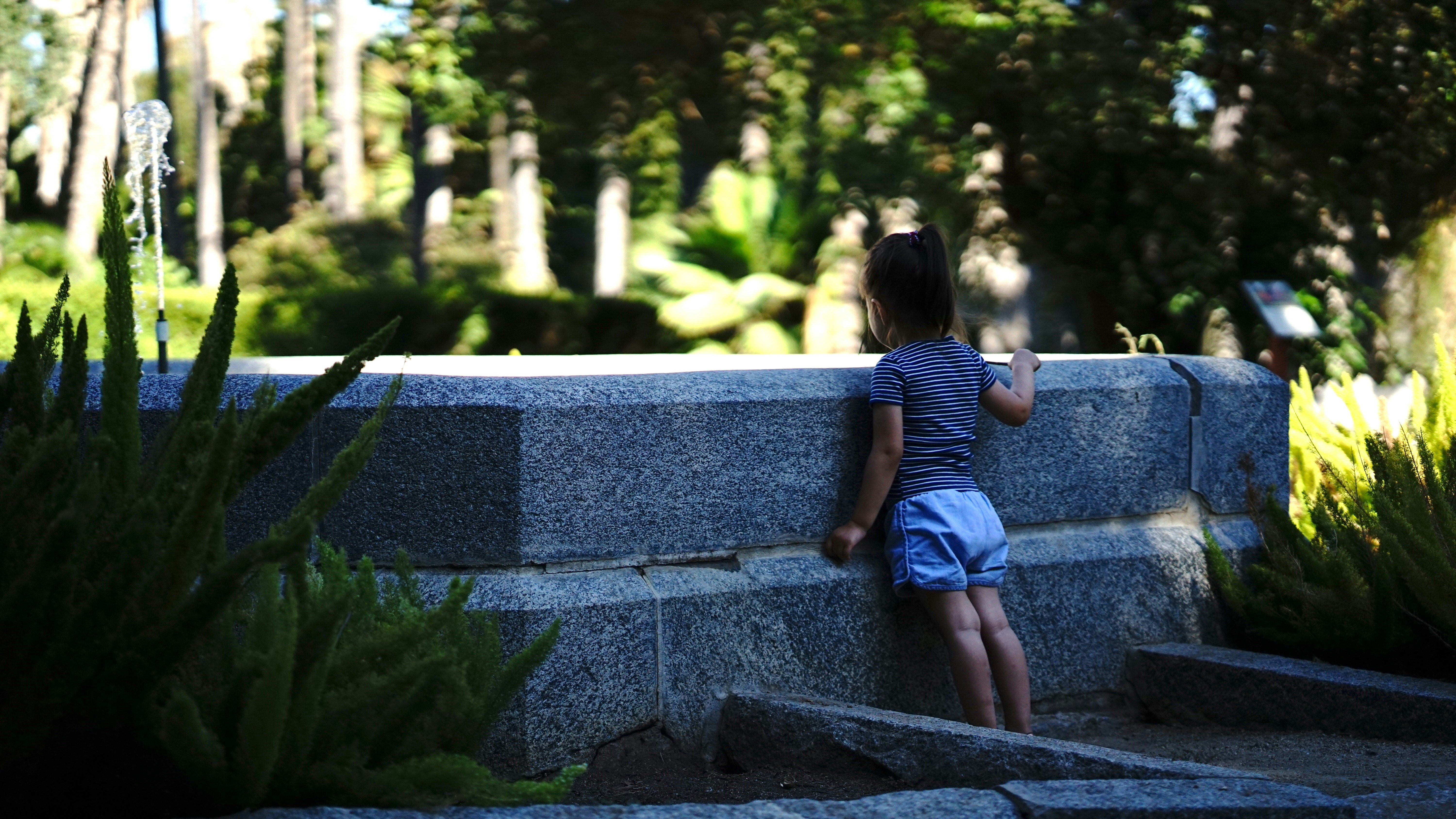 a little girl standing next to a stone wall