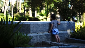 a little girl standing next to a stone wall