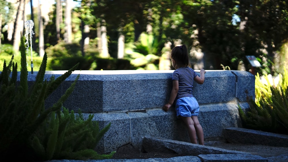 a little girl standing next to a stone wall