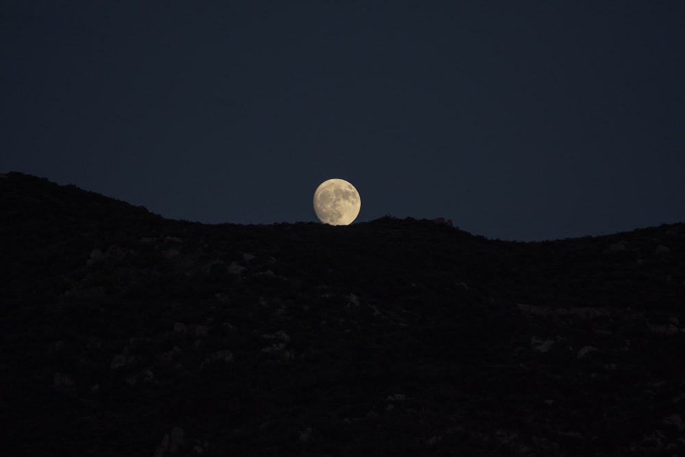 a full moon is seen above a hill