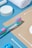 Various toiletries are arranged neatly on a blue and beige background, including a colorful toothbrush, cotton swabs, a white rolled towel, and a round container.