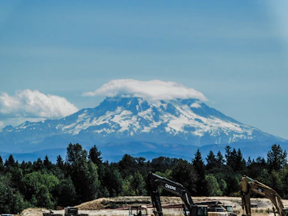 Modern construction equipment stationed on a forested site with mountains in the background.