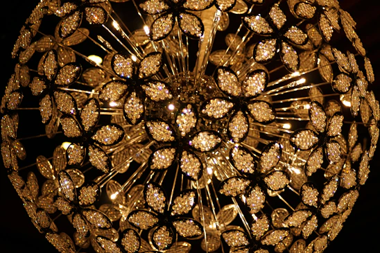 A spherical chandelier composed of numerous crystal flower-like elements arranged in intricate patterns. Each crystal petal reflects light, creating a dazzling and luxurious glow. The composition showcases detailed craftsmanship with sparkling crystals and warm lights emanating from the center.