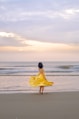 a woman in a yellow dress standing on a beach