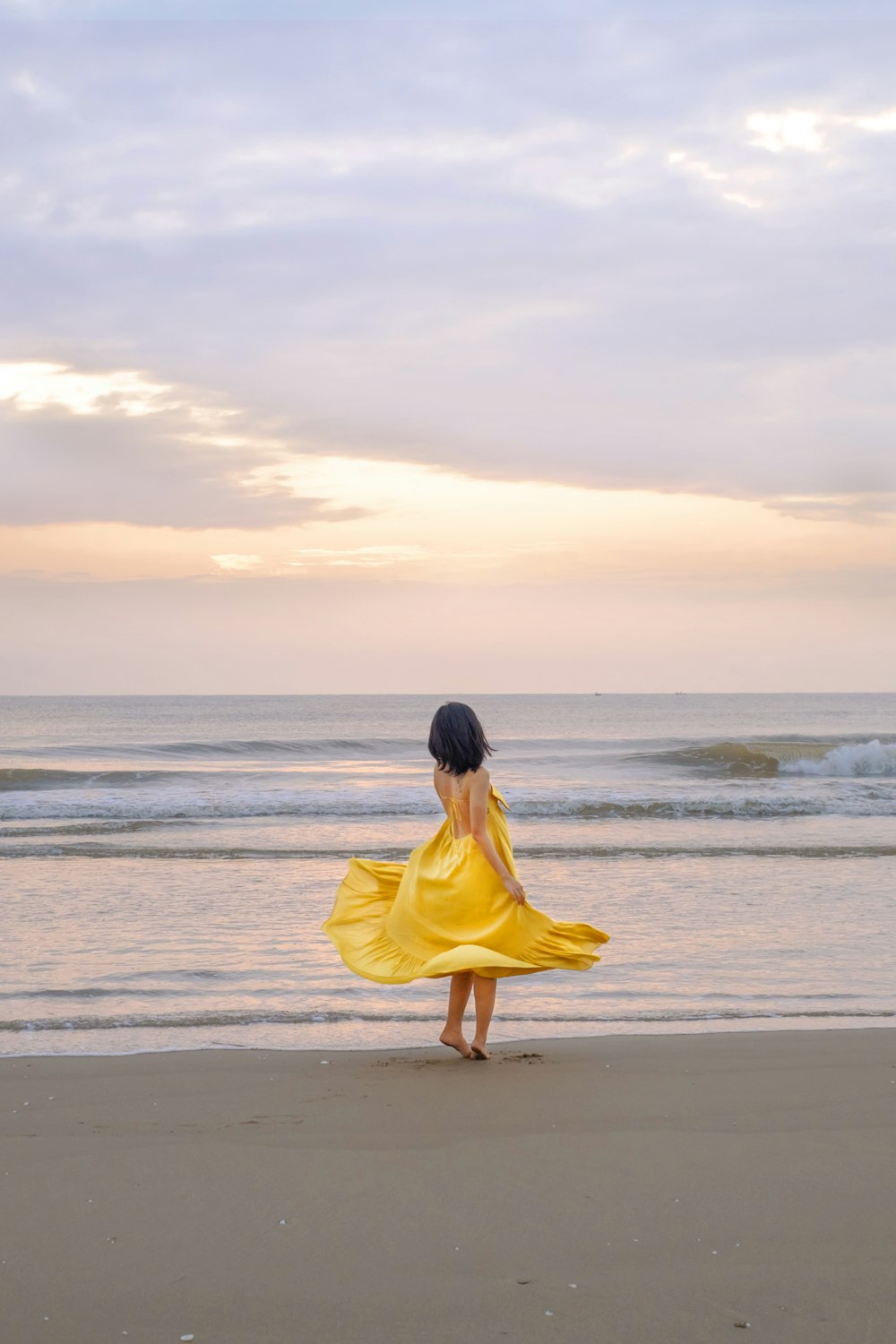 a woman in a yellow dress standing on a beach