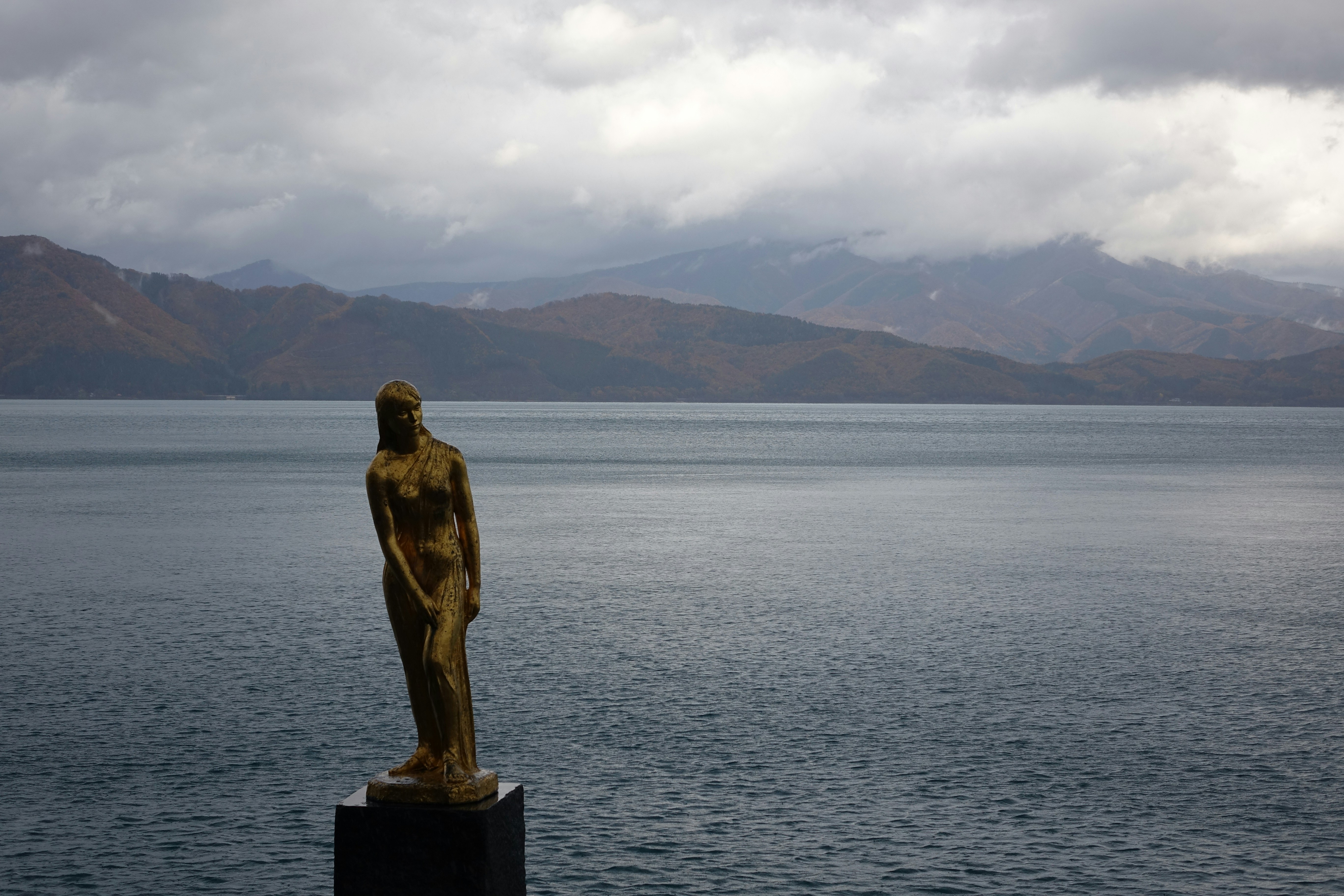 a statue of a woman standing on a pedestal in front of a body of water
