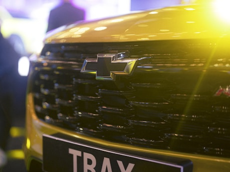 A close-up of the front grille of a Chevrolet car with the Chevrolet logo prominently displayed. The vehicle is yellow, and there is a bright yellow light effect on the right side, adding a dramatic flair.