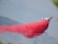 An aircraft discharges a large plume of red fire retardant over a mountainous landscape covered in a haze. The act of releasing the substance creates a striking contrast against the subdued tones of the background, conveying a sense of urgency.