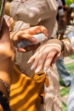 Hands applying a creamy natural lotion outdoors surrounded by greenery.
