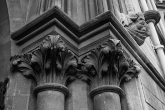 Two intricately carved stone columns with ornate capitals featuring leaf and floral patterns. The columns are part of a larger architectural structure with precise lines and angles, suggesting classical or Gothic influence.