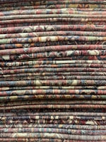 Stack of handloom carpets with varied textures and natural hues ready for shipment.