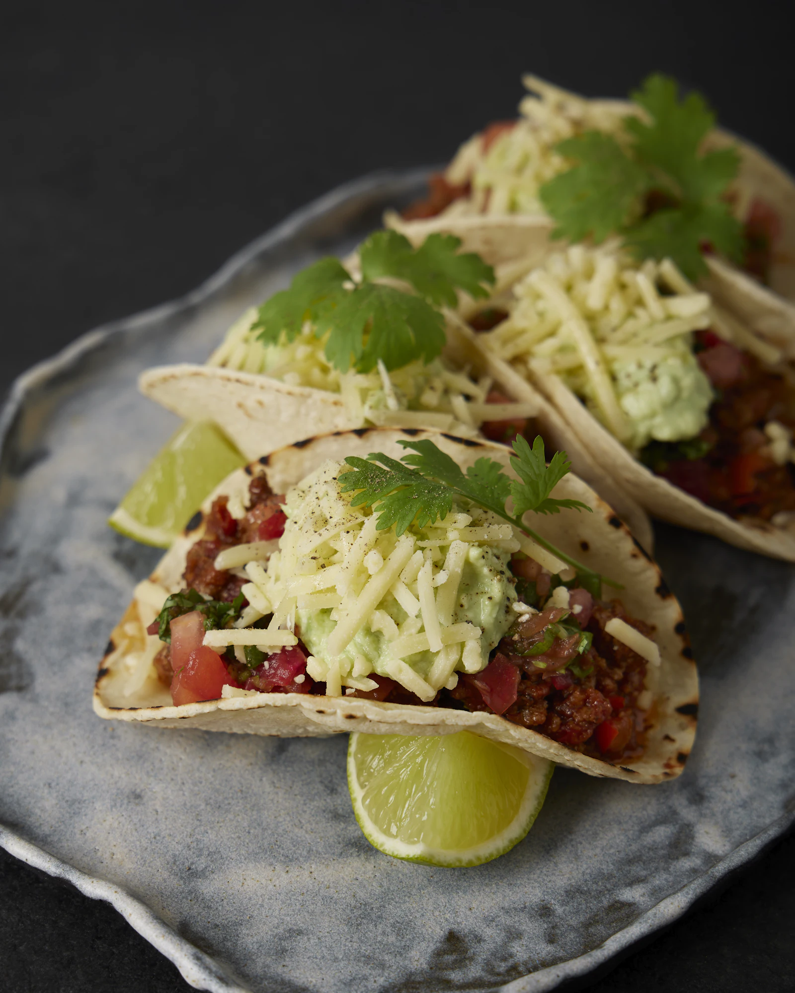 Three tacos on a plate with lime wedges and fresh cilantro