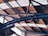 Overhead view of a metal structure with a series of intersecting beams and trusses supporting a corrugated roof, which is partially illuminated by natural light.