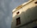 A low-angle view of a beige building with a sign at the top reading 'Khadi India'. The facade features square windows with red frames, and there are shadows cast on the wall, suggesting nearby trees or other structures. The sky is overcast, giving the scene a subdued lighting.