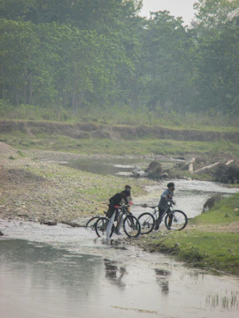Mountain bikers crossing a river with lush green hills in the background