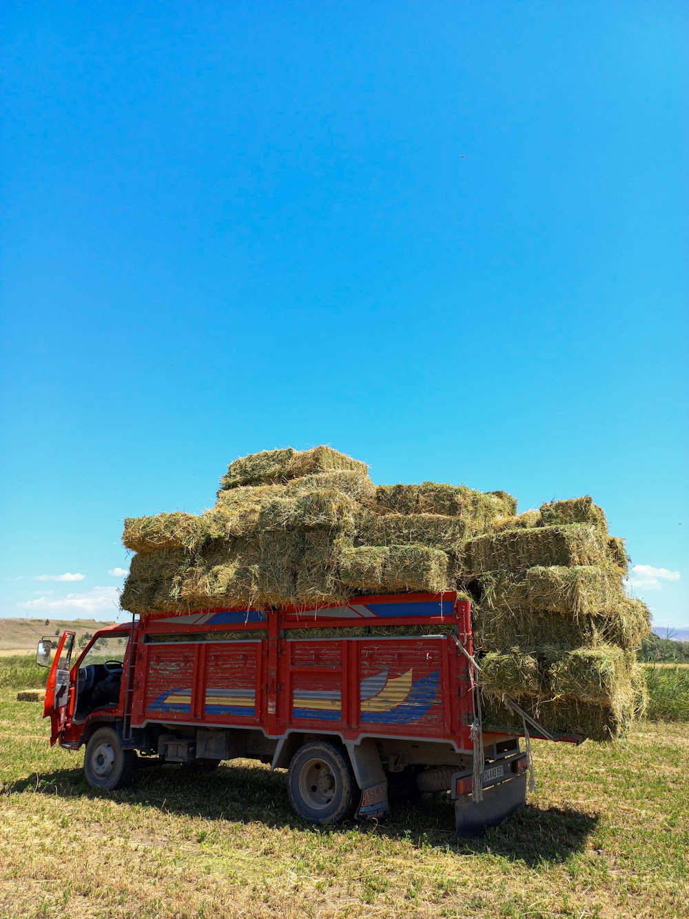 a red truck loaded with hay in a field