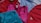 Several sports tank tops in an assortment of colors including red, pink, blue, and turquoise, arranged overlapping one another. The tops feature logos from different brands.