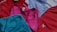 Several sports tank tops in an assortment of colors including red, pink, blue, and turquoise, arranged overlapping one another. The tops feature logos from different brands.