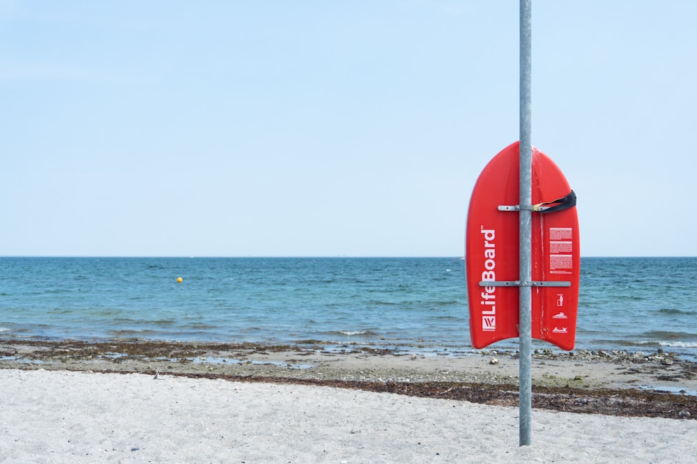 a red surfboard sitting on top of a sandy beach