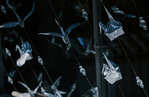Delicate origami birds arranged in a graceful mobile hanging near a sunlit window.