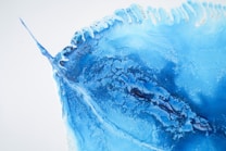A vibrant abstract artwork featuring shades of blue with a texture reminiscent of ocean waves or icy landscapes. The image has an organic flow, with darker blue veins running through the lighter hues, creating a dynamic and fluid appearance.