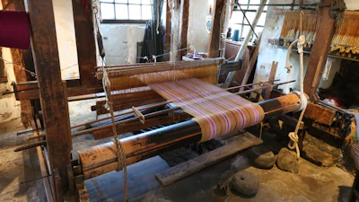 Artist hands weaving vibrant threads on a wooden frame in a sunlit studio.