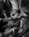 A group of women are gathered around a baby, holding it gently. The baby has a small mark on the cheek and appears to be sucking its thumb. The women's hands are adorned with bangles and rings, suggesting a cultural or family gathering.