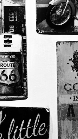 A black and white image featuring vintage-style wall art, including a Route 66 sign, a classic gas pump, and part of a motorcycle wheel. The decor evokes a retro, nostalgic atmosphere.