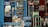 A small shop is filled with various bottled drinks, including Pepsi and Coca-Cola, displayed in coolers and on shelves. Water bottles are stacked on counters and in crates. A man sits nearby, wearing a mix of colorful and subdued clothing, adding a lived-in feel to the scene.