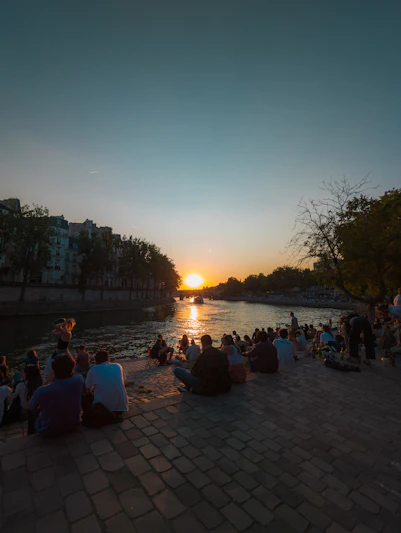 A warm gathering of community members praying together by the riverside at sunset.