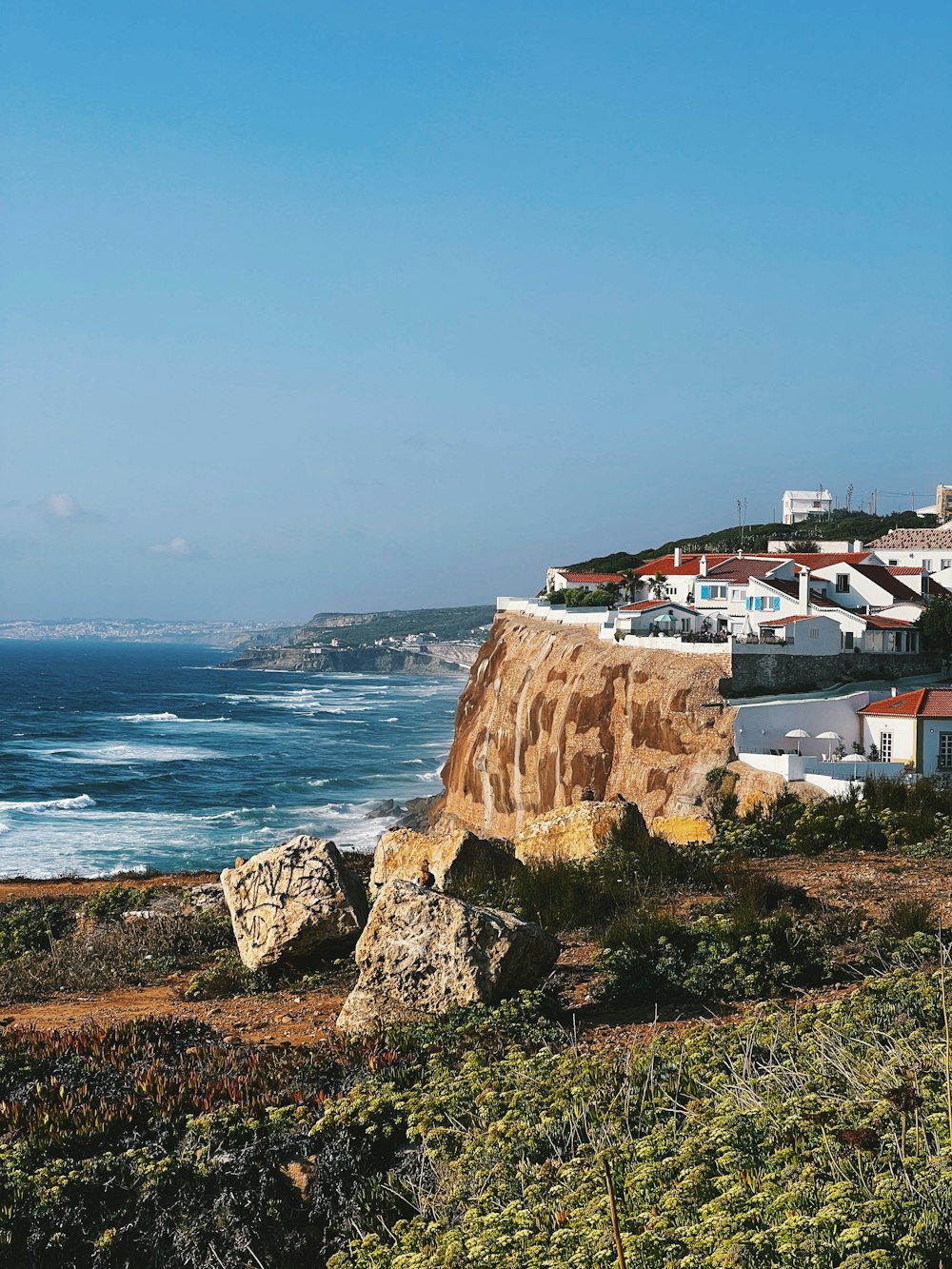 a view of a beach with houses on the cliff