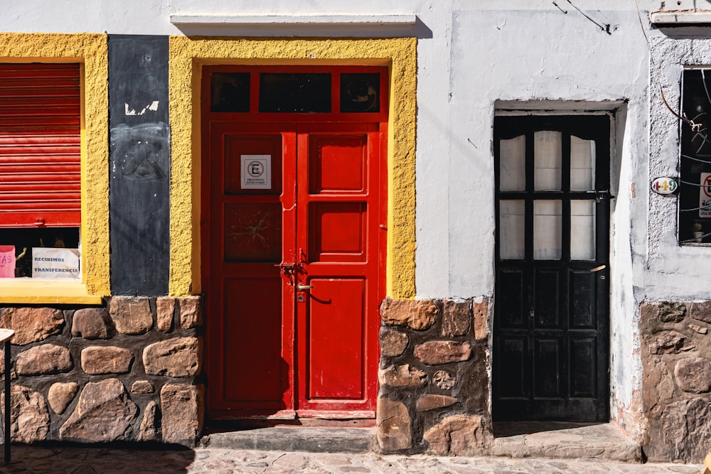 a red door on a white building with yellow shutters