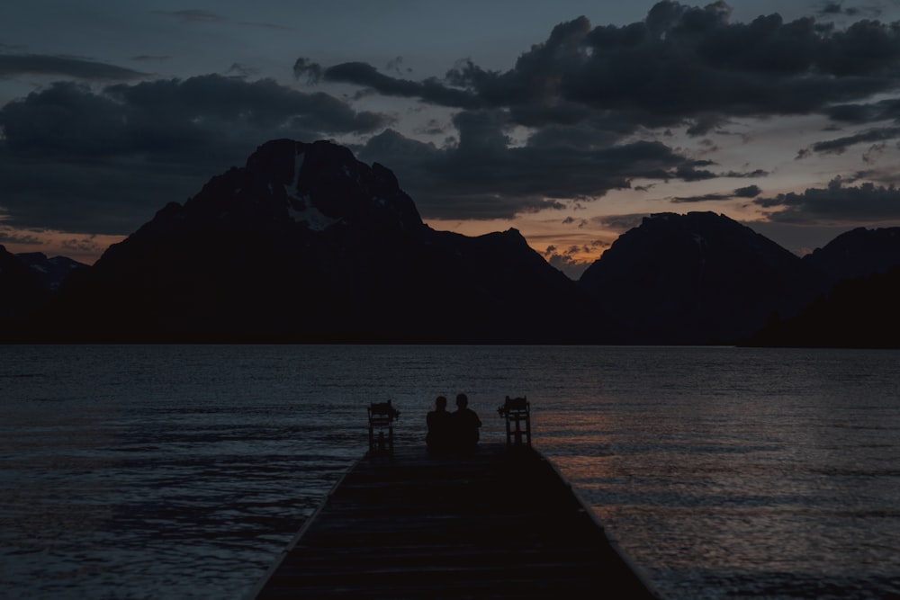 two people sitting on a dock watching the sunset