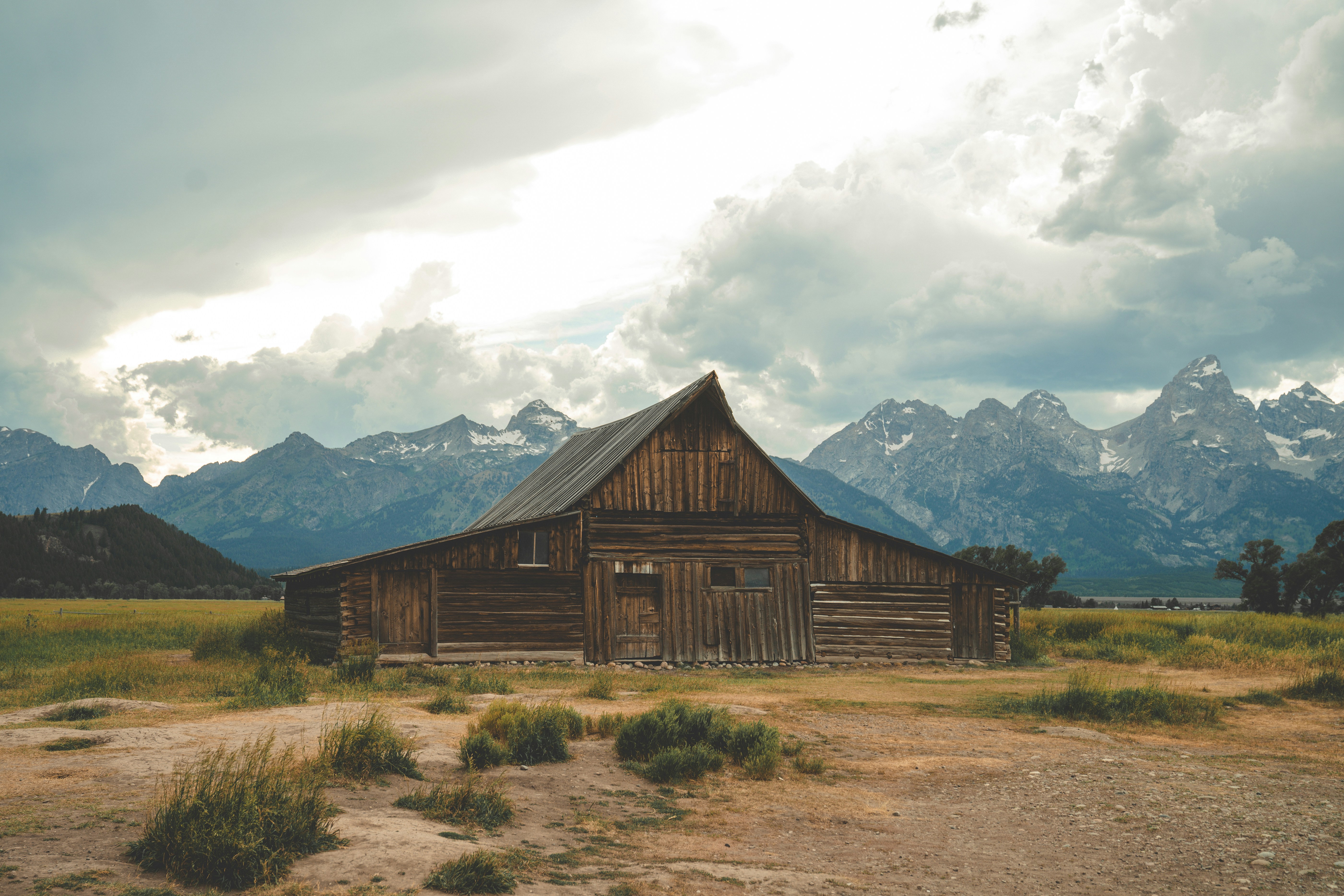 an old barn in a field with mountains in the background